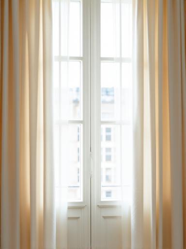 Elegante tendaggio su misura in seta color avorio che drappeggia lussuosamente di fronte a una finestra.